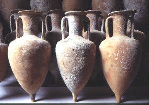 Fila di anfore romane in terracotta esposte su uno scaffale museale.